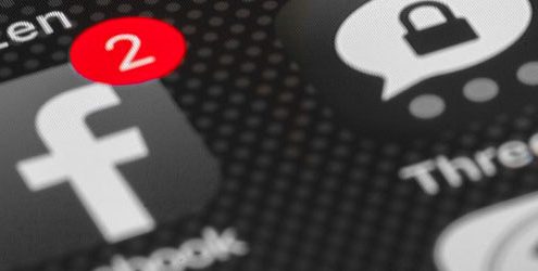 Schermata di iPhone in bianco e nero e notifica push, associata all'icona di Facebook, di colore rosso e che indica il numero due