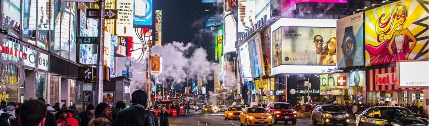 Strada affollata di una grande città con macchine e pareti dei grattacieli coperte di schermi che passano pubblicità