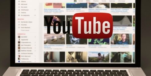 Canale YouTube Aziendale: laptop aperto su una pagina di YouTube con logo della piattaforma in sovraimpressione su sfondo grigio