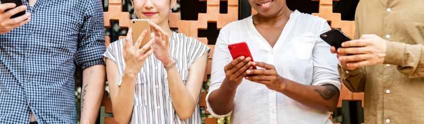 Due ragazze e due ragazzi in fila che guardano sorridendo lo smartphone che hanno tra le mani