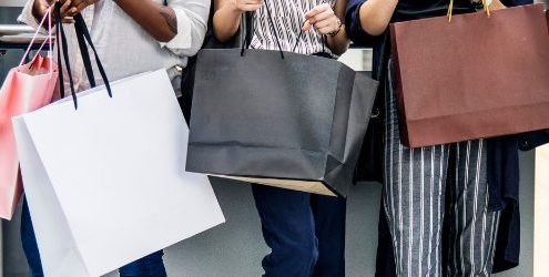 Consumatore: ragazzi e ragazza in fila con buste degli acquisti fra le mani