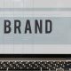 promuovere la tua azienda: schermo di laptop che mostra la parola brand, laptop poggiato su un tavolo con vicino una tazza usa e getta di caffè e un paio di cuffie