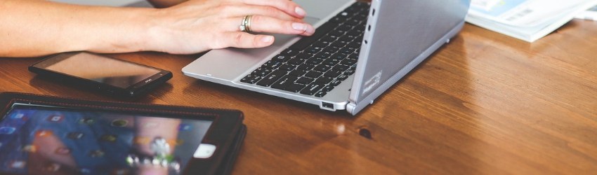smartphone pieghevoli: mani di donna che digitano su una tastiera di un pc con accanto un tablet e uno smartphone