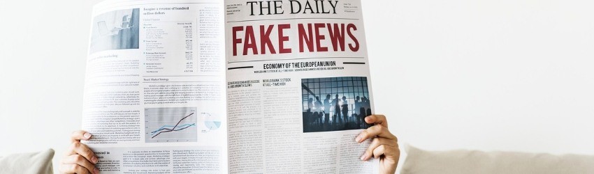 Fake News Elezioni Europee: donna che tiene un giornale aperto davanti al volto con scritto Fake News in prima pagina